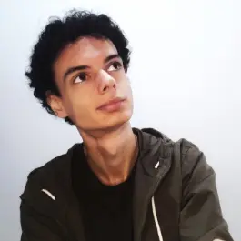 Júlio looking up-right, on a white background, with a short curly dark brown hair, looking up, wearing a green jacket and t-shirt.